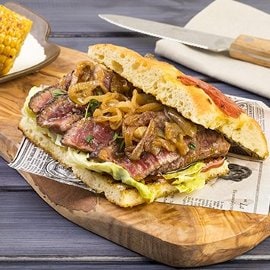 Focaccia di patate con tagliata di manzo laccato alla BBQ dolce e sambuca con pannocchia di mais al sale maldon e cipolle arrostite al rosmarino Focaccia di patate con tagliata di manzo laccato alla BBQ dolce e sambuca con pannocchia di mais al sale maldon e cipolle arrostite al rosmarino